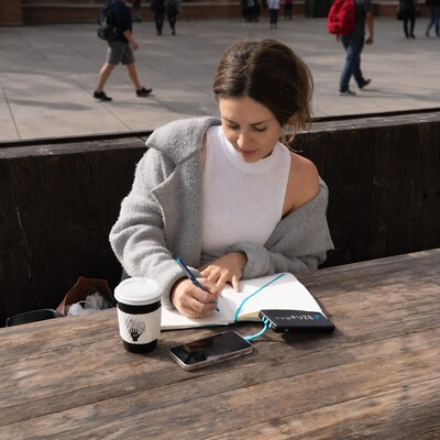 College student writing in a notebook outdoors on campus with a chargeFUZE portable charger keeping her phone powered. College student writing in a notebook outdoors on campus with a chargeFUZE portable charger keeping her phone powered.