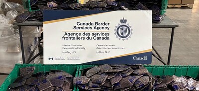 A large quantity of sealed cocaine packages displayed in green totes with a CBSA poster. The drugs were seized by Canada Border Services Agency officers in Halifax, NS in March 2026. (CNW Group/Royal Canadian Mounted Police - Central Region)