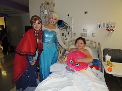 Costumed characters, Elsa and Anna from Frozen, spread holiday joy and deliver a plush toy to Miller Children's patient, Kayla.