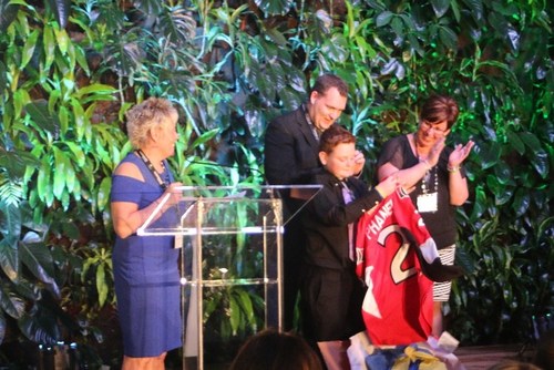 WISHES COME TRUE Colin Gillespie (centre) shows off an Ottawa Senators jersey – one of the items from his wish box –  presented by Event Coordinator, Sylvia Densmore (left), as he is applauded by his parents, James (centre) and Laurie Gillespie (right). (CNW Group/The Children's Wish Foundation of Canada)