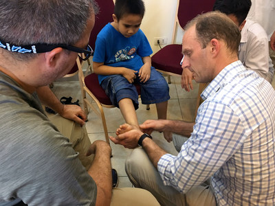 AOFAS volunteer surgeons Lorenzo Gamez, MD (left) and Geoffrey M. Tymms, MBBS (right) examine a young patient at the Vinh Orthopedics Rehab Center in Vinh, Vietnam.​