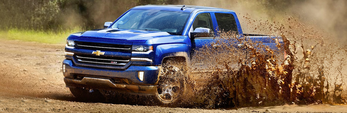 Blue Chevrolet Silverado 1500 driving splashing up a wave of mud.