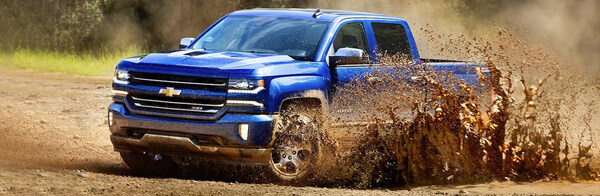 Blue Chevrolet Silverado 1500 driving splashing up a wave of mud.