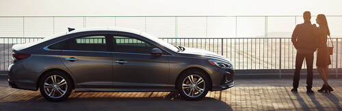 View of a couple standing arm in arm next to the 2018 Hyundai Sonata at dusk.