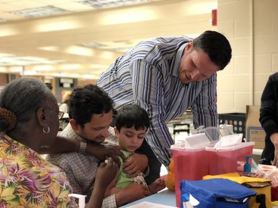 Tony Boselli (right) looks on as a child at the Healthy Schools Emergency Flu Shot Clinic at Mandarin High School receives a flu shot. Healthy Schools vaccinates all kids regardless of insurance status.