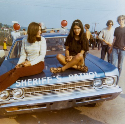 Two young women relax on the hood of a Sheriff’s Patrol car at the corner of Hwy. 17B and Hurd Road as people begin to flock into the Woodstock festival. Photo by Elizabeth Alexander. Bethel Woods Collection, gift of Elizabeth Alexander.