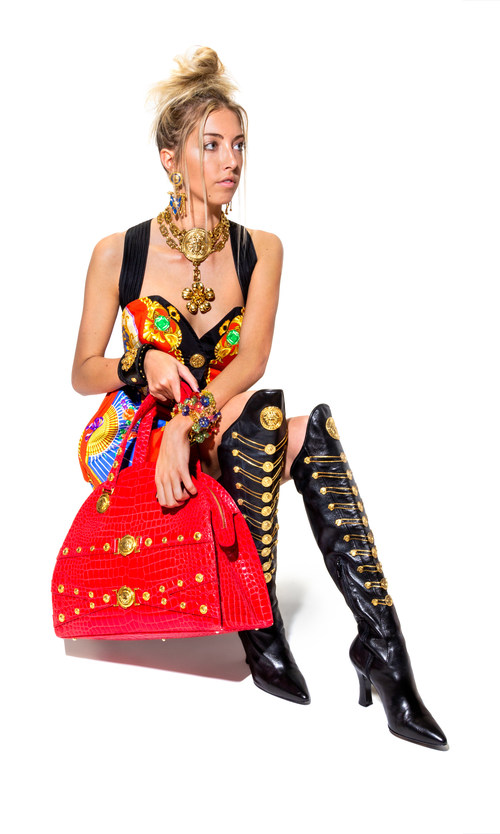 Items to be offered September 21 at Leslie Hindman Auctioneers' The Genius of Gianni Versace auction, modeled by Hannah Warner. Items include blue enamel flag drop earclips; a runway choker; a silk Atelier print mini dress (design from the Spring 1991 runway); a red crocodile embossed Medusa bag; a multicolor floral and Greco link bracelet; and black leather chain boots. The entire collection includes over 350 Gianni Versace designs from the 90s, brought to auction by a single owner.