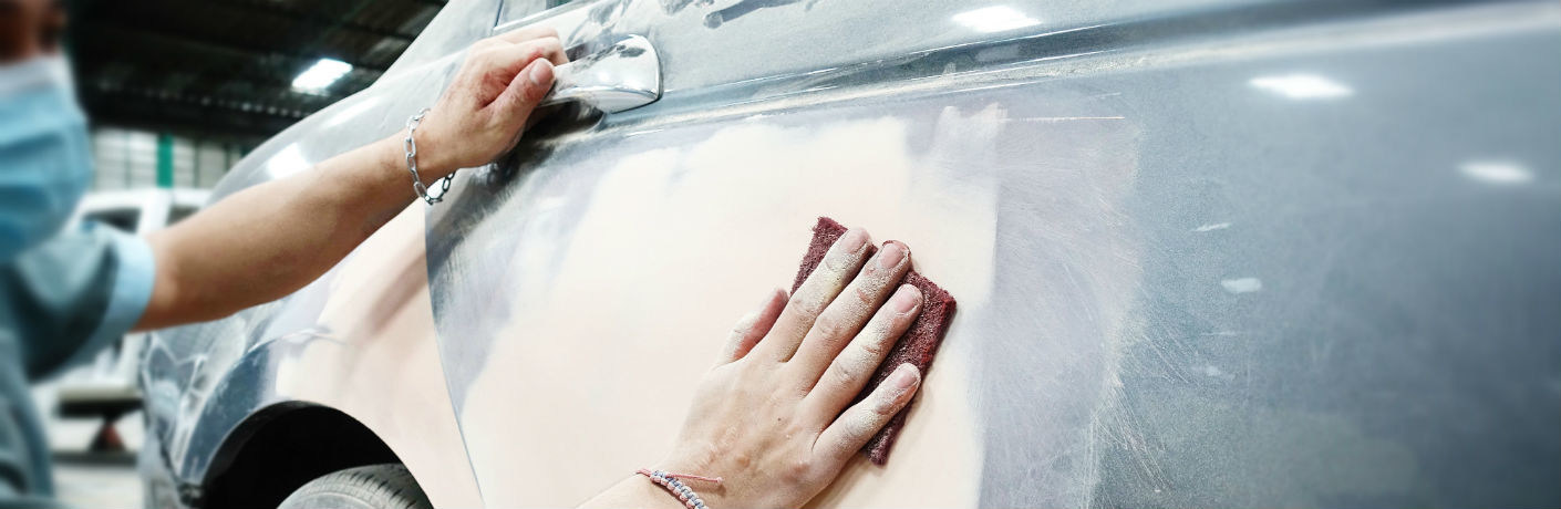 Body shop technician spreads bondo overa damaged car