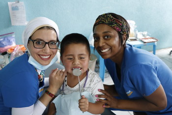 Dr. Reham El-Hennawey, endodontist, and Yara Almedia, dental assistant, with a local young boy providing dental care.