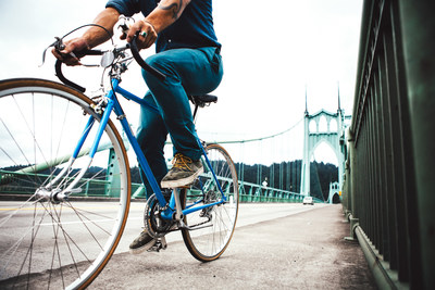An unrecognizable man commuting across the St John's Bridge in an urban city environment. He travels on his street bicycle into the city over the Saint John's Bridge. No face visible. Horizontal with copy space. (CNW Group/WESTJET, an Alberta Partnership)