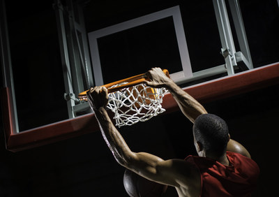 Rear-view shot of a young basketball player in a red jersey in mid-air taking a dunk shot, with both hands clothing the ring.