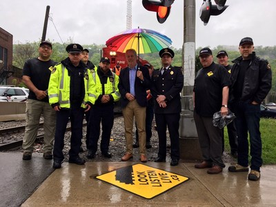 Hamilton’s Mayor Fred Eisenberger (centre, holding umbrella) and Dave Thompson of Hamilton Paramedic Service (right of Mayor) are joined by CP Police Service and CP Operations and Engineering employees to unveil the city’s first “Look.Listen.Live” sidewalk decal at the Cumberland Avenue crossing by Gage Ave S. (CNW Group/Canadian Pacific)