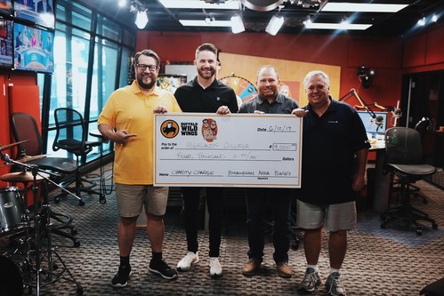 Pastor Mark Pettus stands with hosts Rick Burgess and Bubba Bussey as Buffalo Wild Wings representative Tim Spencer presents Highlands College a $4,000 check.