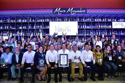 Mezcaleros y dignatarios estaban jubilosos en la ceremonia donde se anunció que Oaxaca había ganado el Récord Guinness con el “Muro Mezcalero” en Vive Mezcal, Foro Internacional. En la primera fila, al centro de izquierda a derecha, empezando con la representante de Guinness: Natalia Ramírez, Récords Mundiales de Guinness, adjudicadora; Juan Carlos Guzmán Cobián, secretario de la Economía de Oaxaca; Alejandro Murat Hinojosa, gobernador de Oaxaca; Dante Montano, alcalde de Santa Lucía del Camino; y Juan Carlos Rivera Castellanos, secretario de Turismo de Oaxaca.